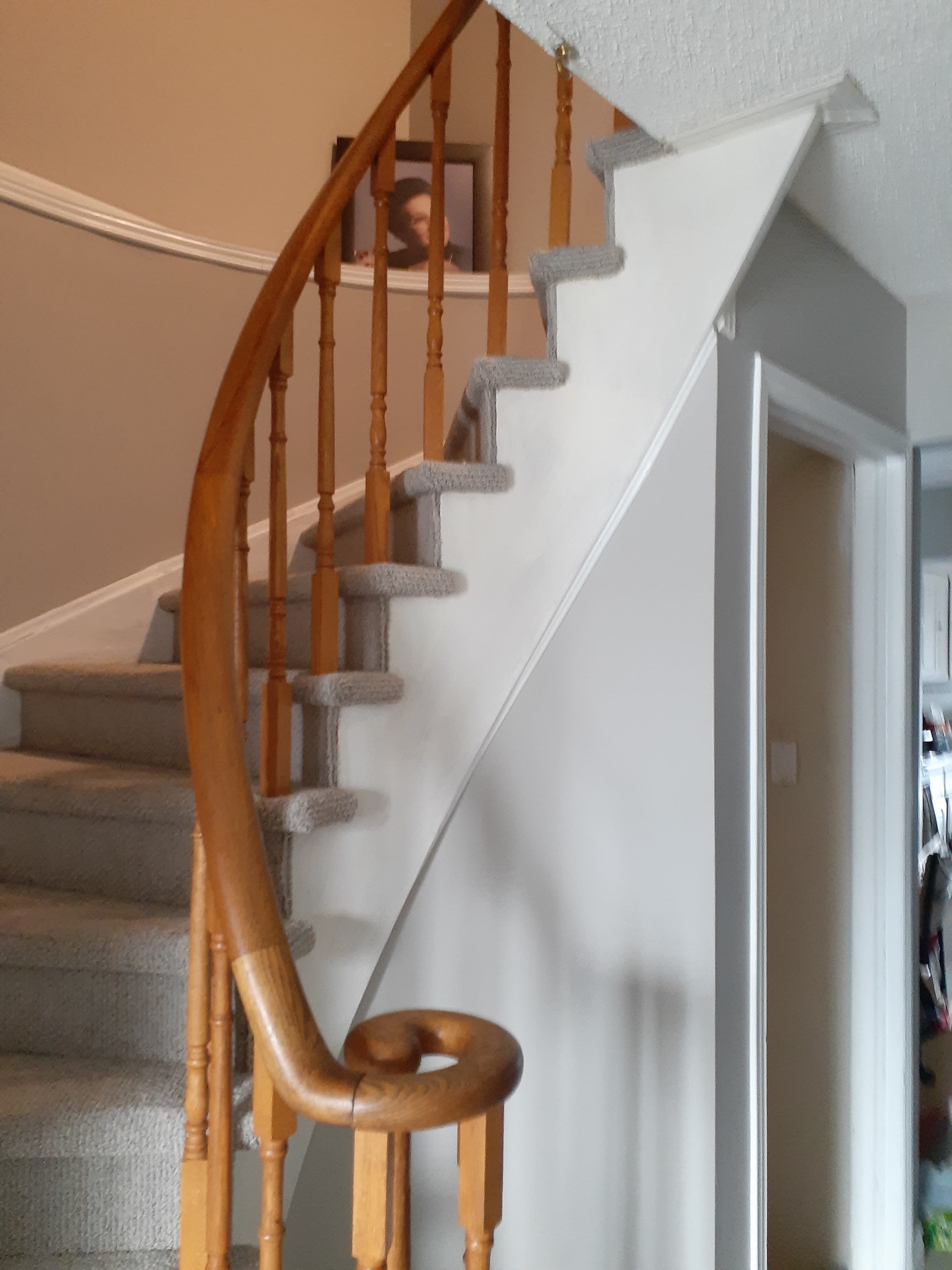 Curved staircase with wood handrail and carpet before painting refresh